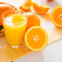 Vaso de zumo de naranja fresco acompañado de naranjas recién cortadas de Valencia.