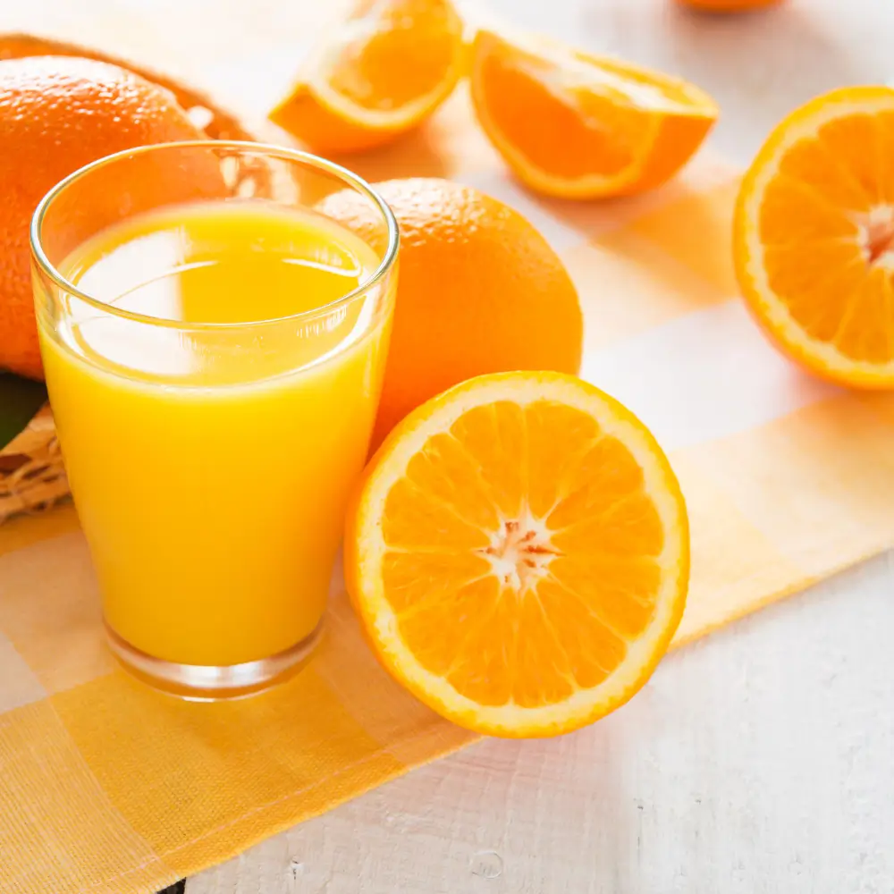 Vaso de zumo de naranja fresco acompañado de naranjas recién cortadas de Valencia.