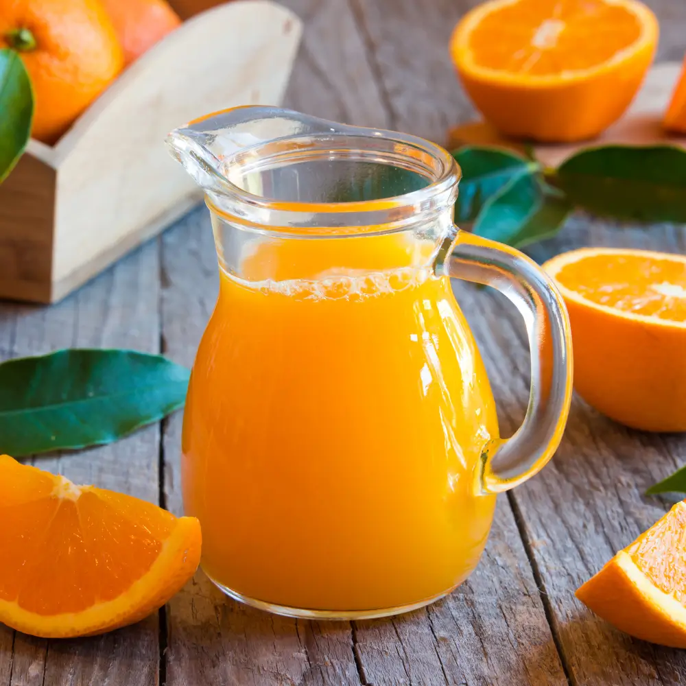 Jarra de zumo de naranja recién exprimido con naranjas cortadas sobre una mesa de madera rústica.