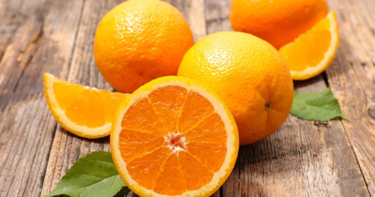 Naranjas Valencia Late sobre tabla rústica con hojas verdes y una naranja cortada